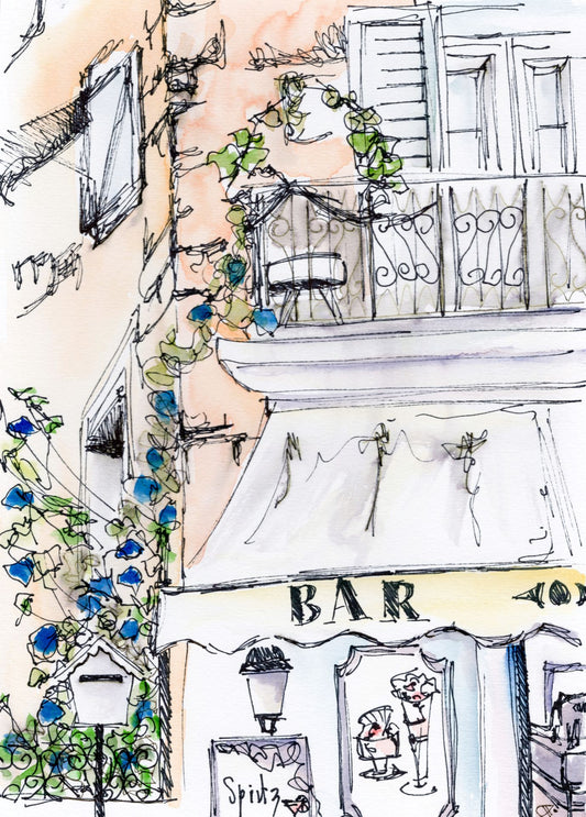 Cafe scene of a bar in Propriano, Corsica. Orange building with blue flowers on climbing plant with balcony above the Bar awning. A sign displaying 'Spritz' and ice creams on a framed board.